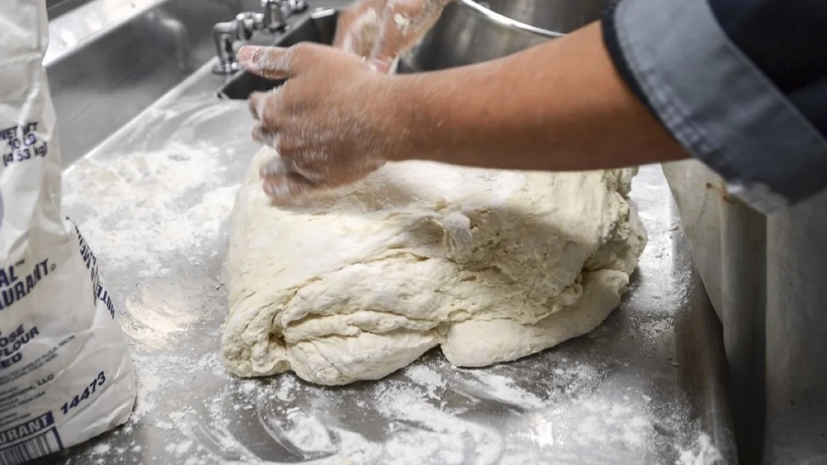 Soft enriched bread dough being kneaded by hand on a work surface