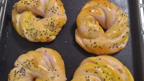 天板に並んだ、ねじって輪にしたさつまいもパン。照りと黒ごまがかかっている