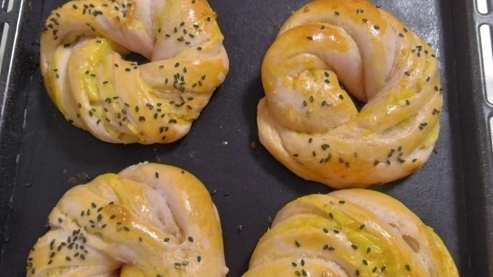 天板に並んだ、ねじって輪にしたさつまいもパン。照りと黒ごまがかかっている