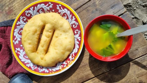 赤い皿にのったきつね色のチベタン・ブレッド（中央に切れ目）と、青菜の入ったスープ